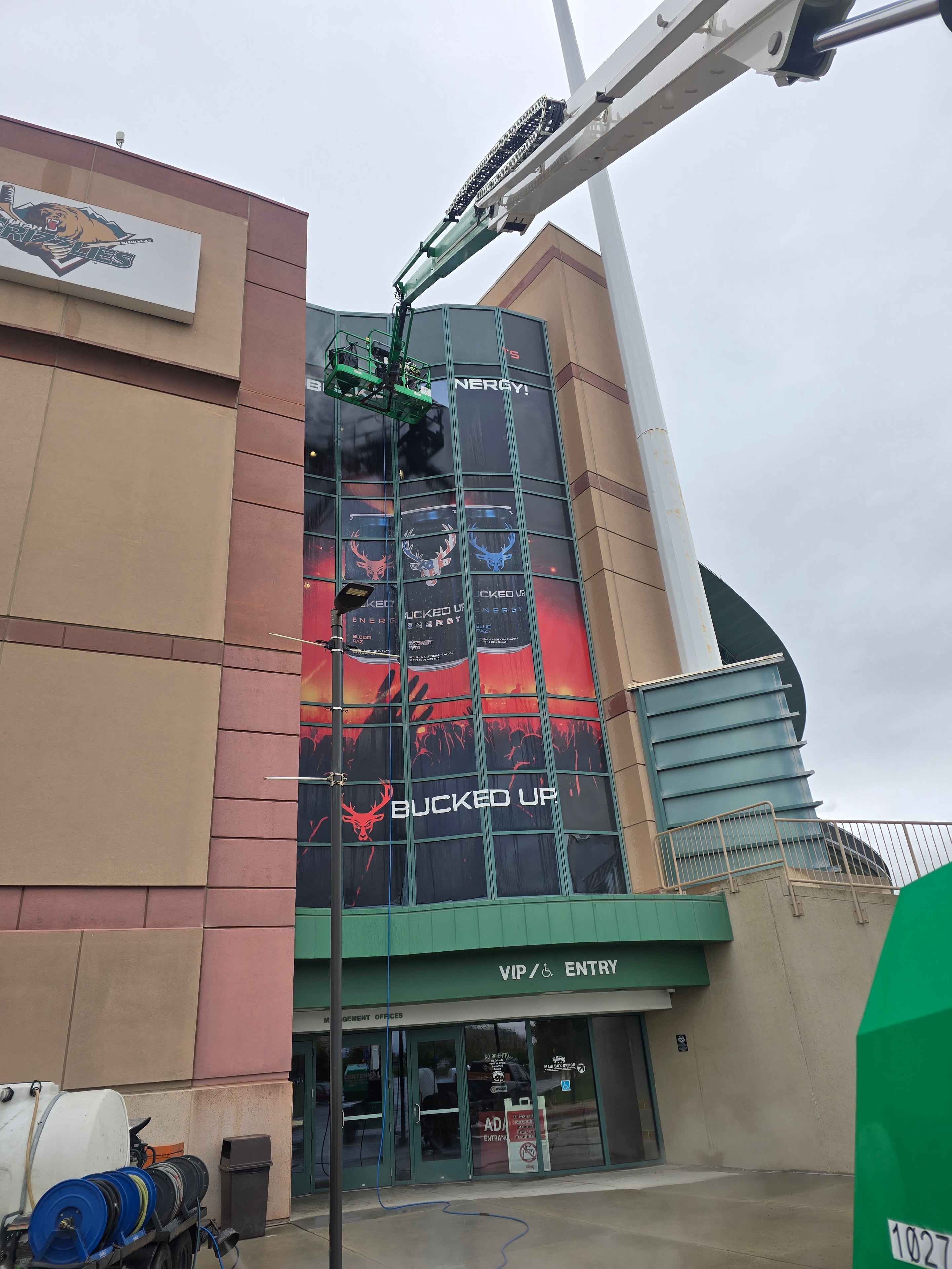 Boom lift extended to Bucked Up window wrap on Maverick Center facade during cleaning — wide shot