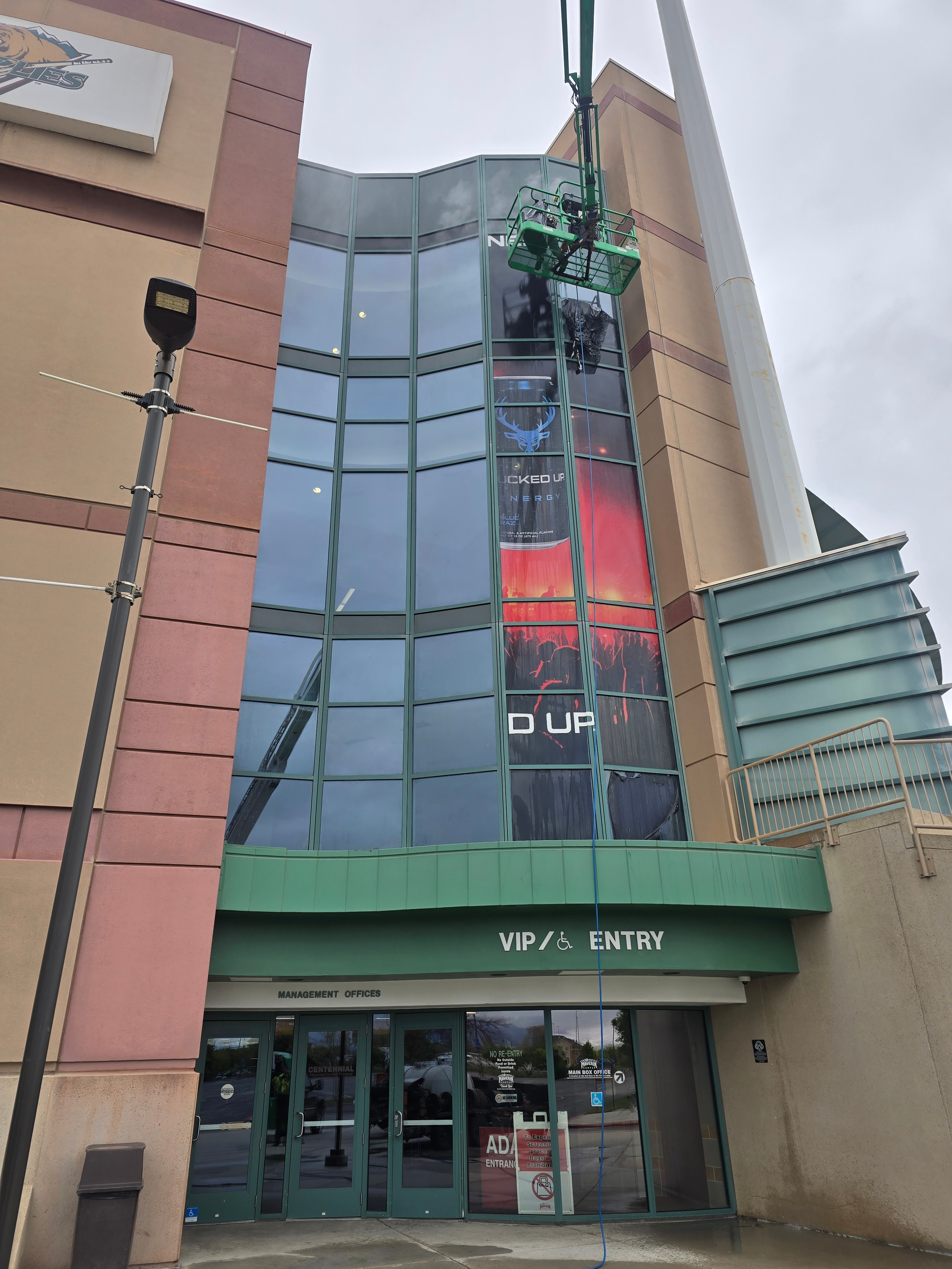 Angled view of boom lift cleaning Bucked Up arena wrap — Maverick Center, West Valley City